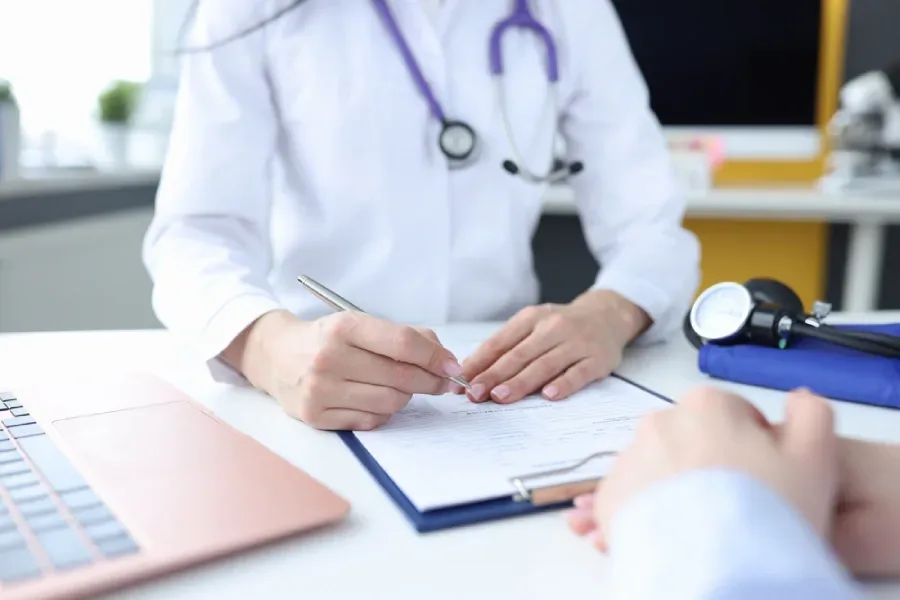 Doctor sitting with patient at a desk and writing on a clipboard