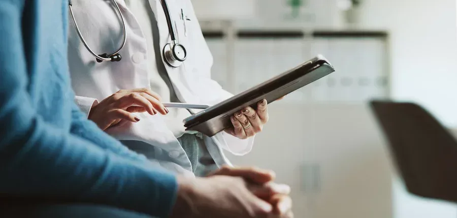 A doctor consults a tablet while meeting with a patient.