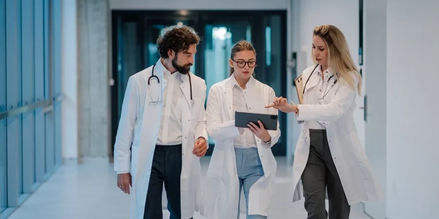A group of young doctors reviews healthcare data on a tablet while walking through a hospital corridor.
