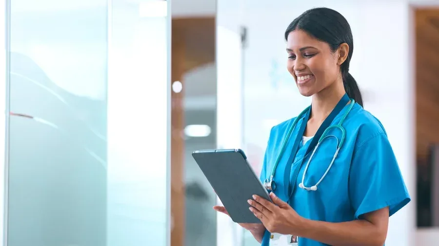 A smiling nurse accesses data on a tablet.