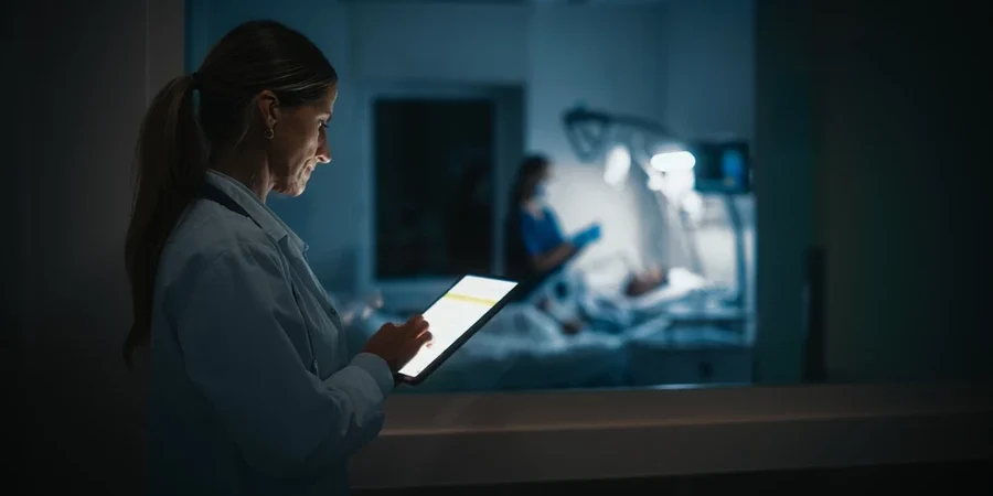 A clinician accesses data on a tablet outside of a patient's room at night.